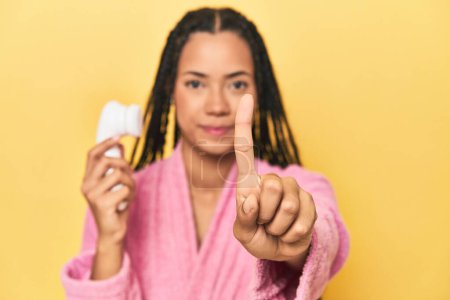 Téléchargez les photos : Indonésien femme avec nettoyant pour le visage sur jaune montrant numéro un avec doigt. - en image libre de droit