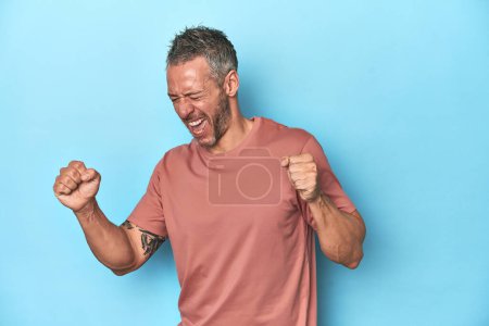 Foto de Hombre caucásico de mediana edad sobre fondo azul bailando y divirtiéndose. - Imagen libre de derechos