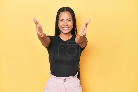 Téléchargez les photos : Jeune femme indonésienne sur fond de studio jaune montrant une expression bienvenue. - en image libre de droit