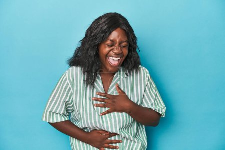 Téléchargez les photos : Jeune femme courbée afro-américaine rit joyeusement et s'amuse à garder les mains sur l'estomac. - en image libre de droit