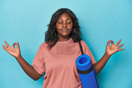 Photo for Curvy woman ready to practice yoga on a blue backdrop - Royalty Free Image
