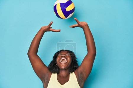 Foto de Deportiva mujer con curvas practicando voleibol sirve en telón de fondo azul - Imagen libre de derechos