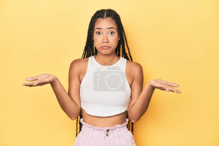Photo for Young Indonesian woman on yellow studio backdrop doubting and shrugging shoulders in questioning gesture. - Royalty Free Image