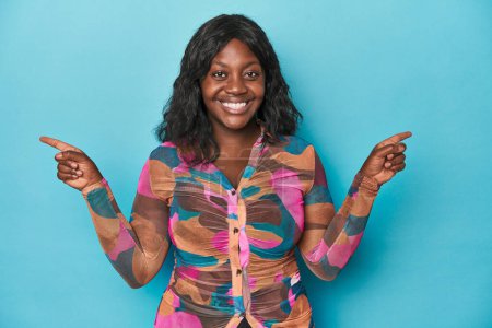 Téléchargez les photos : Jeune femme courbée afro-américaine pointant vers différents espaces de copie, en choisissant l'un d'eux, montrant avec le doigt. - en image libre de droit