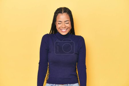 Photo for Young Indonesian woman on yellow studio backdrop laughs and closes eyes, feels relaxed and happy. - Royalty Free Image