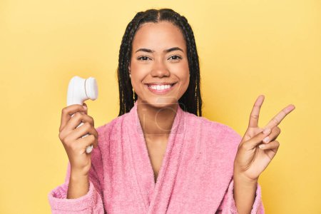 Téléchargez les photos : Indonésien femme avec nettoyant pour le visage sur jaune montrant numéro deux avec les doigts. - en image libre de droit