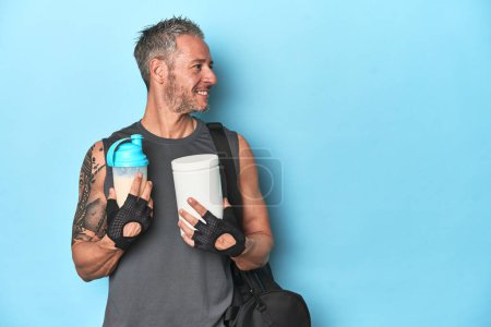 Téléchargez les photos : Athlète tenant shake protéine et récipient sur fond bleu - en image libre de droit
