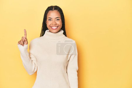 Foto de Joven mujer indonesia en el fondo del estudio amarillo mostrando el número uno con el dedo. - Imagen libre de derechos