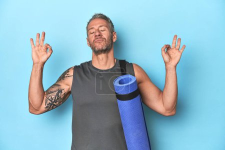 Téléchargez les photos : Athlète tenant un tapis de fitness sur fond bleu studio - en image libre de droit