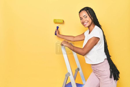 Foto de Mujer indonesia pintando pared con escalera y rodillo en amarillo - Imagen libre de derechos