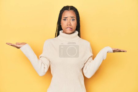 Téléchargez les photos : Jeune femme indonésienne sur fond jaune studio épaules confuses et douteuses haussant les épaules pour tenir un espace de copie. - en image libre de droit