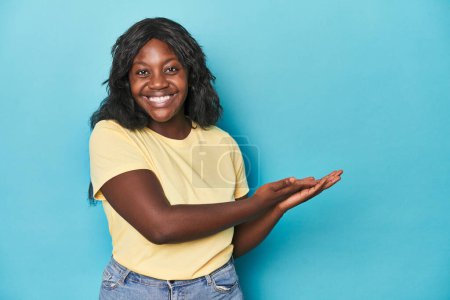 Foto de Joven mujer con curvas afroamericana sosteniendo un espacio de copia en una palma. - Imagen libre de derechos