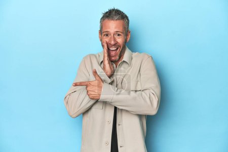 Photo for Middle-aged caucasian man on blue backdrop saying a gossip, pointing to side reporting something. - Royalty Free Image