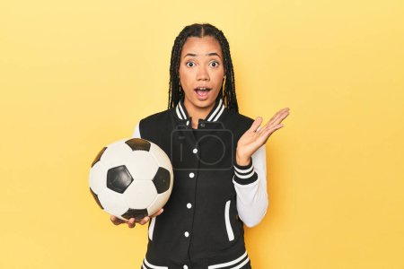 Photo for Indonesian schoolgirl with soccer ball on yellow surprised and shocked. - Royalty Free Image