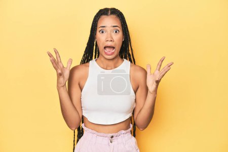 Photo for Young Indonesian woman on yellow studio backdrop screaming to the sky, looking up, frustrated. - Royalty Free Image