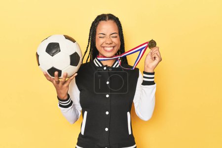 Photo for Young Indonesian woman with medal and soccer ball on yellow studio background - Royalty Free Image