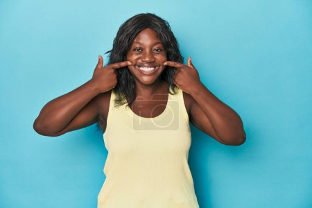 Téléchargez les photos : Jeune femme afro-américaine courbée sourit, pointant du doigt la bouche. - en image libre de droit