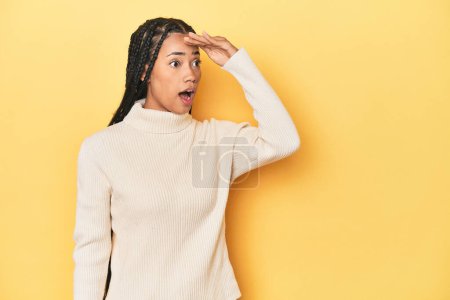 Photo for Young Indonesian woman on yellow studio backdrop looking far away keeping hand on forehead. - Royalty Free Image