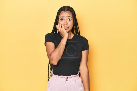 Photo for Young Indonesian woman on yellow studio backdrop biting fingernails, nervous and very anxious. - Royalty Free Image