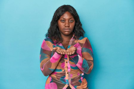 Téléchargez les photos : Jeune femme courbée afro-américaine tenant quelque chose avec des paumes, offrant à la caméra. - en image libre de droit