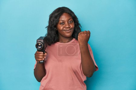 Téléchargez les photos : Dame courbée avec caméra de film vintage montrant poing à caméra, expression faciale agressive. - en image libre de droit