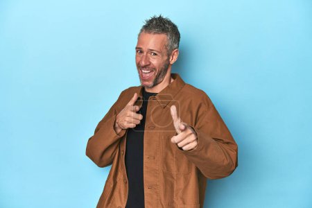 Photo for Middle-aged caucasian man on blue backdrop pointing to front with fingers. - Royalty Free Image
