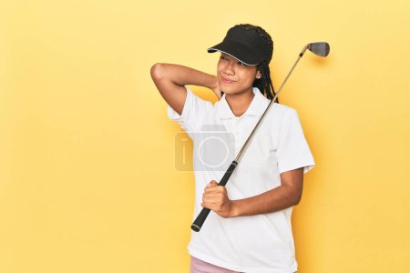 Photo for Indonesian female golfer on yellow backdrop touching back of head, thinking and making a choice. - Royalty Free Image