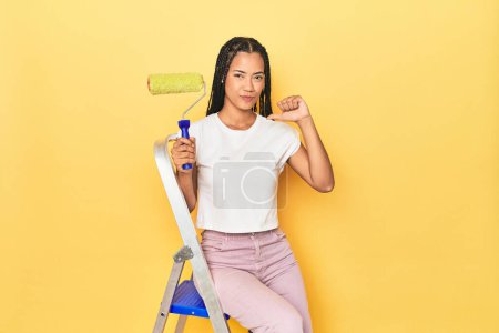 Téléchargez les photos : Femme indonésienne avec rouleau sur l'échelle sur jaune se sent fier et confiant, exemple à suivre. - en image libre de droit