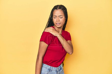 Photo for Young Indonesian woman on yellow studio backdrop having a shoulder pain. - Royalty Free Image