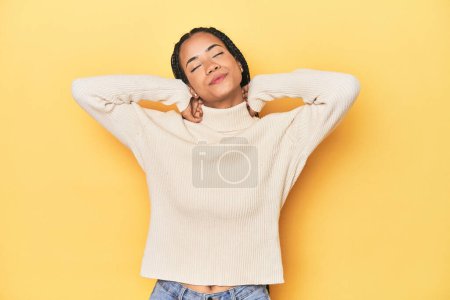 Photo for Young Indonesian woman on yellow studio backdrop feeling confident, with hands behind the head. - Royalty Free Image
