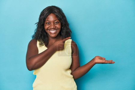 Foto de Joven africana americana curvilínea excitada sosteniendo un espacio de copia en la palma. - Imagen libre de derechos