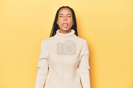 Foto de Joven mujer indonesia en amarillo estudio telón de fondo divertido y amigable sobresaliendo lengua. - Imagen libre de derechos
