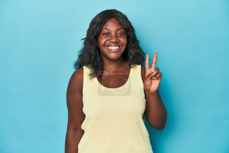 Téléchargez les photos : Jeune femme courbée afro-américaine montrant un signe de victoire et souriant largement. - en image libre de droit