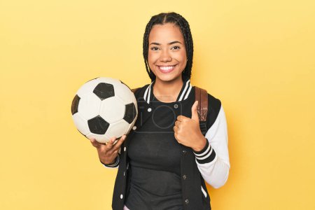 Foto de Colegiala indonesia con pelota de fútbol en amarillo sonriendo y levantando el pulgar hacia arriba - Imagen libre de derechos