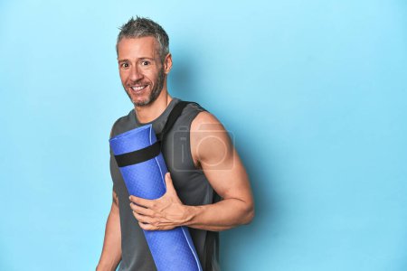 Photo for Athlete holding a fitness mat on blue studio background - Royalty Free Image