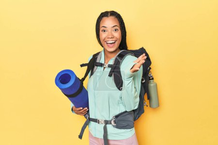 Photo for Indonesian woman ready for mountain trip on yellow receiving a pleasant surprise, excited and raising hands. - Royalty Free Image