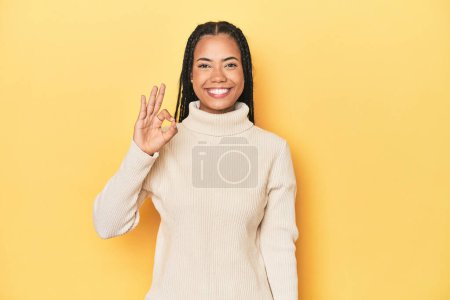 Photo for Young Indonesian woman on yellow studio backdrop cheerful and confident showing ok gesture. - Royalty Free Image