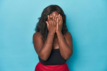 Foto de Joven africana americana curvilínea mujer parpadear a través de los dedos asustado y nervioso. - Imagen libre de derechos