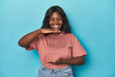 Téléchargez les photos : Jeune femme courbée afro-américaine tenant quelque chose avec les deux mains, présentation du produit. - en image libre de droit