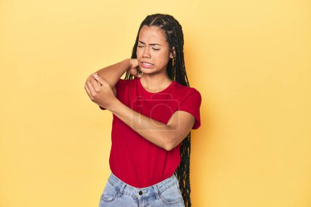Photo for Young Indonesian woman on yellow studio backdrop massaging elbow, suffering after a bad movement. - Royalty Free Image