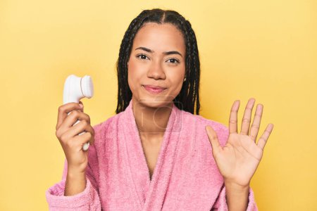 Téléchargez les photos : Femme indonésienne avec nettoyant facial sur jaune souriant gai montrant numéro cinq avec les doigts. - en image libre de droit