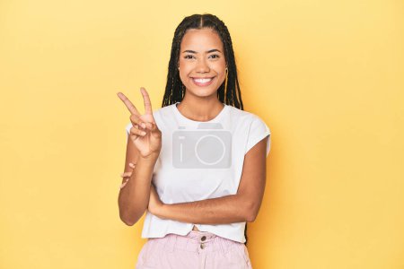 Téléchargez les photos : Jeune Indonésienne sur fond de studio jaune montrant numéro deux avec les doigts. - en image libre de droit