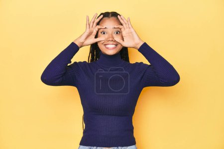Photo for Young Indonesian woman on yellow studio backdrop keeping eyes opened to find a success opportunity. - Royalty Free Image