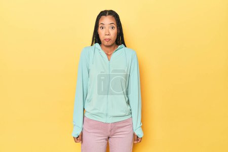 Photo for Indonesian sporty woman on yellow backdrop shrugs shoulders and open eyes confused. - Royalty Free Image