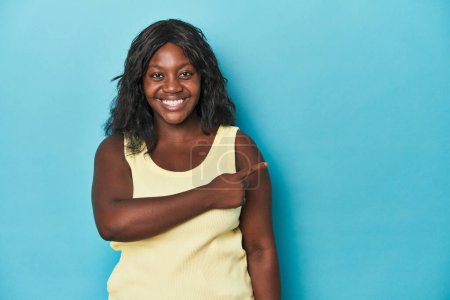 Téléchargez les photos : Jeune femme courbée afro-américaine souriante et pointant du doigt, montrant quelque chose à vide. - en image libre de droit