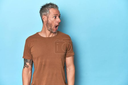 Foto de Hombre caucásico de mediana edad sobre fondo azul siendo sorprendido por algo que ella ha visto. - Imagen libre de derechos