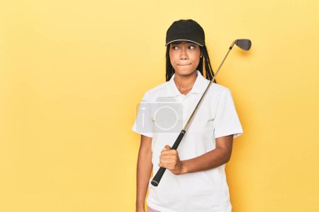 Photo for Indonesian female golfer on yellow backdrop confused, feels doubtful and unsure. - Royalty Free Image