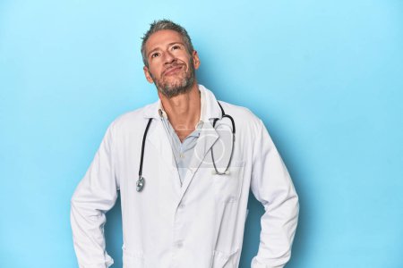 Photo for Caucasian middle-aged doctor on blue background dreaming of achieving goals and purposes - Royalty Free Image