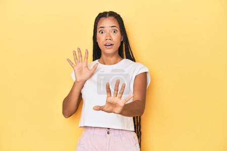 Photo for Young Indonesian woman on yellow studio backdrop being shocked due to an imminent danger - Royalty Free Image
