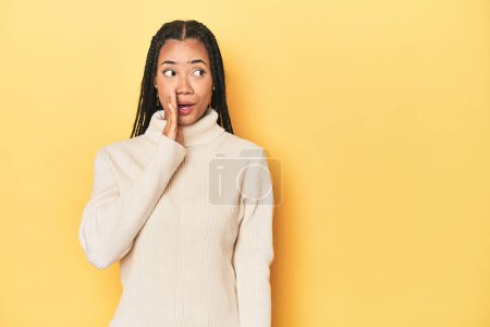Photo for Young Indonesian woman on yellow studio backdrop is saying a secret hot braking news and looking aside - Royalty Free Image